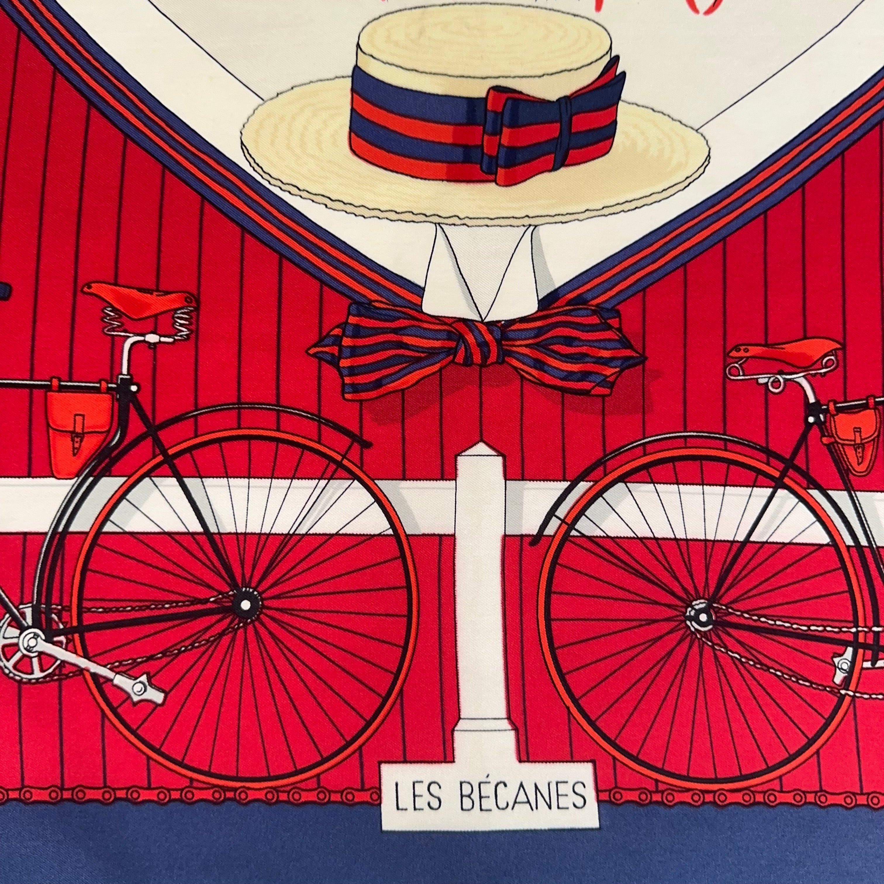 Zoom sur le médaillon central : un canotier (chapeau de paille) décoré d'un ruban bleu et rouge au-dessus d'un nœud papillon.