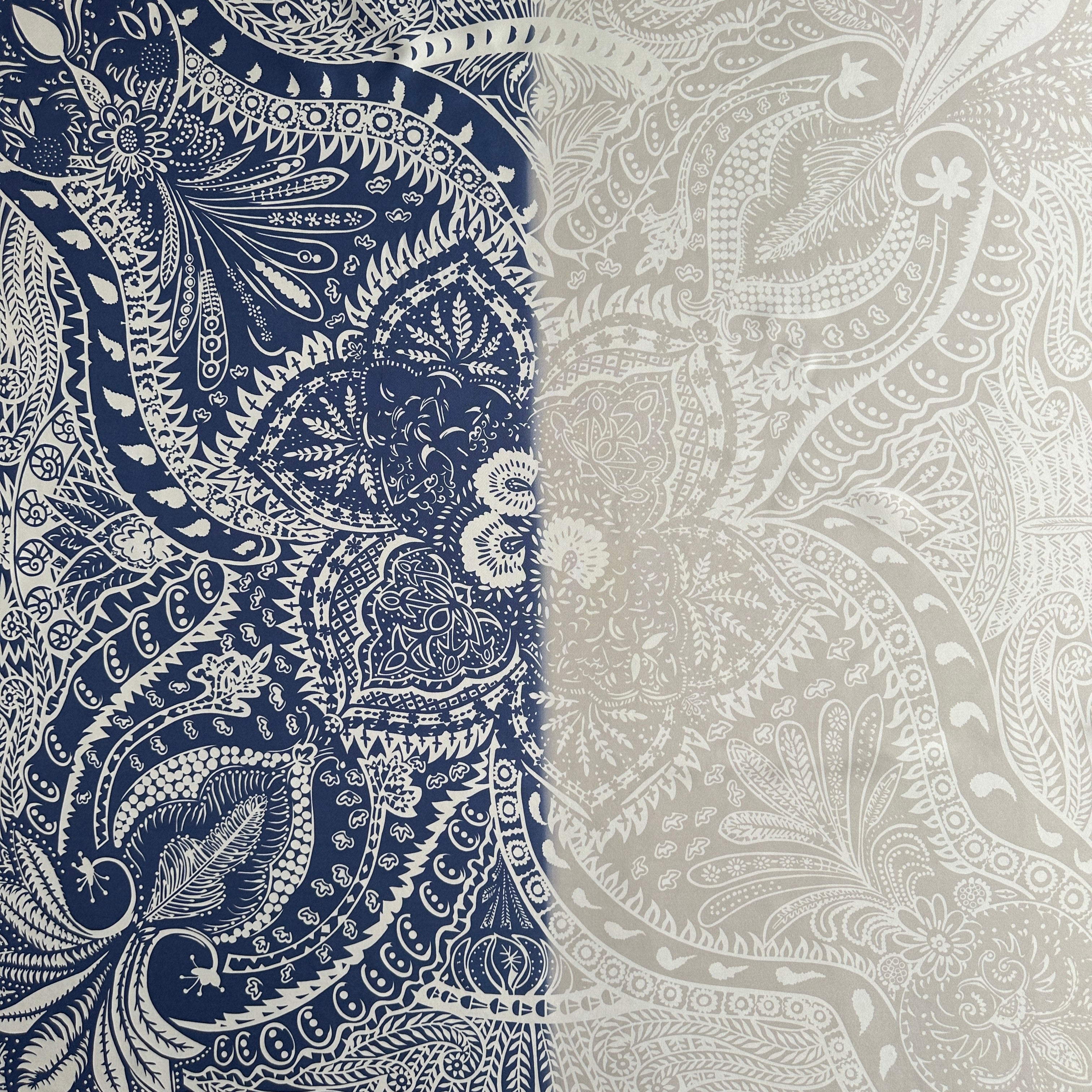 Gros plan sur la transition de couleur du foulard Hermès, montrant le motif paisley blanc continu passant du fond bleu marine au fond gris clair.