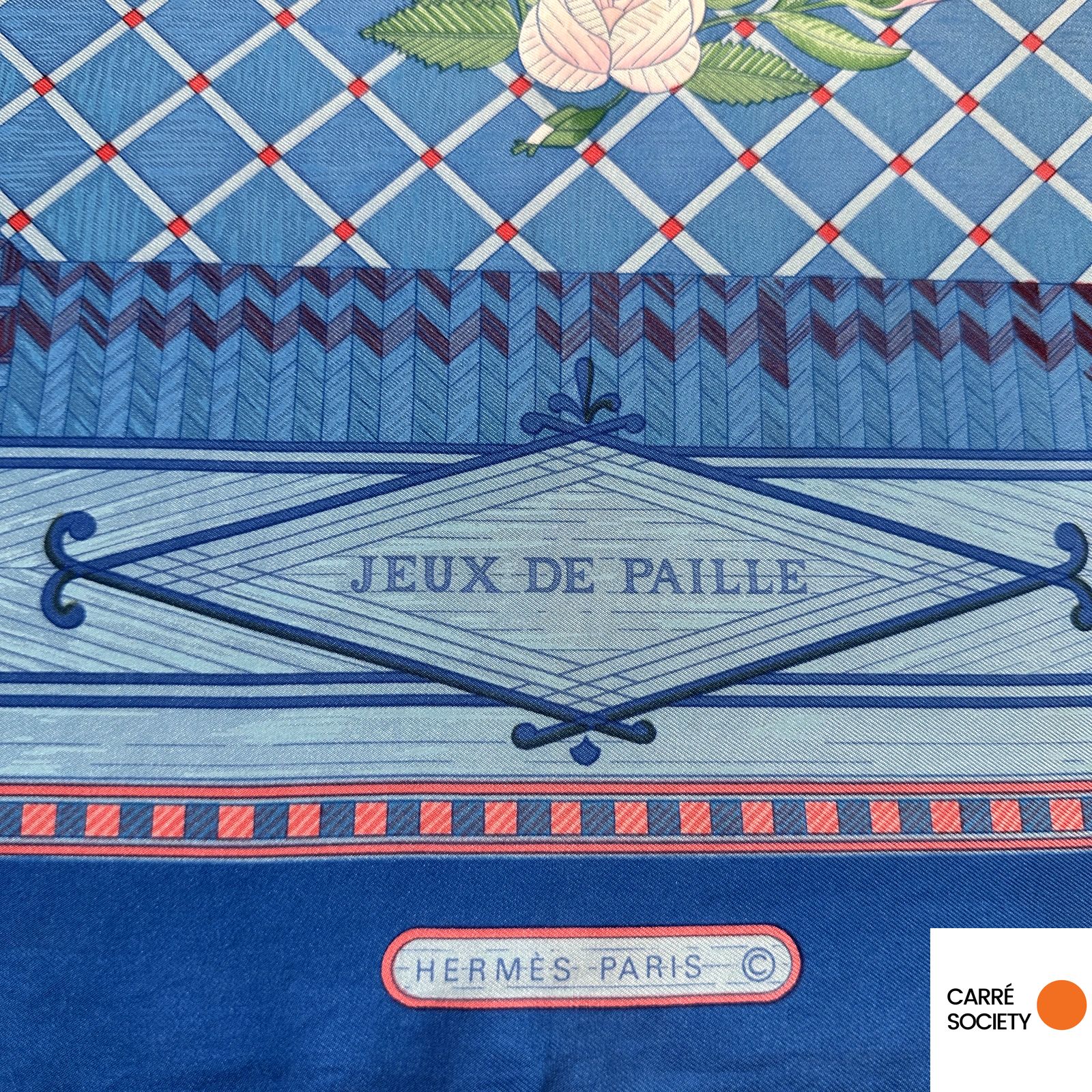 Détail du titre Jeux de Paille et de la mention Hermès Paris imprimés sur le foulard Hermès, avec bordure à motif damier rouge et bleu.